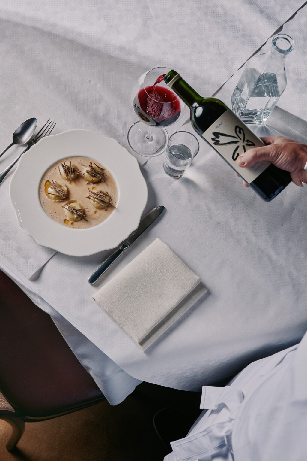 En portion tryffelravioli på ett bord med vit duk och ett glas rödvin hälls upp i glas.