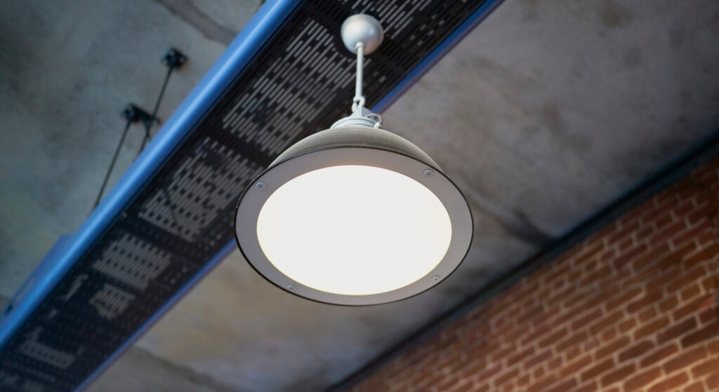 Ensam taklampa lyser. Väggen består av rött tegel.