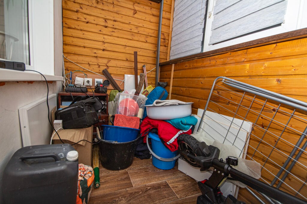 En balkong full av hinkar, dunkar, en cykel och annat skräp.