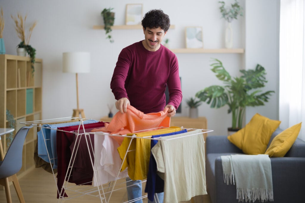 Glad man i vinröd tröja hänger upp tvätt på tvättställ i sitt vardagsrum.