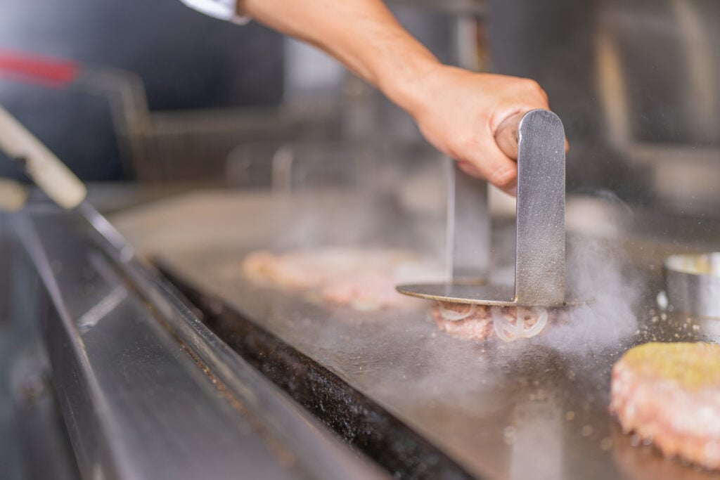 Hamburgare smashas mot stekbord och stekos stiger uppåt.