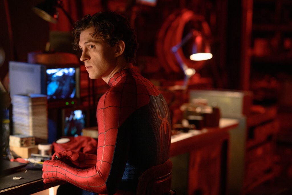 Tom Holland som Spider-Man utan mask. Han står vid ett svagt upplyst arbetsbord och tittar åt sidan.